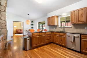 Kitchen featuring wood finish cabinetry, dark stone counters, stainless steel dishwasher, and lofted ceiling