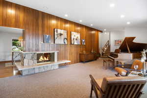 Living room featuring wood walls, a stone fireplace, carpet floors, and recessed lighting