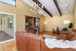 Living room with light wood-style flooring, suspended lighting, vaulted ceiling, and wallpapered walls