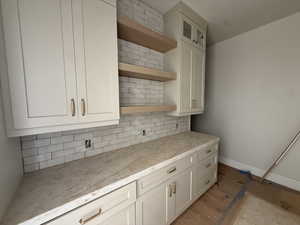 Kitchen with open shelves, tasteful backsplash, glass insert cabinets, and white cabinetry
