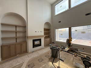 Living room featuring a glass covered fireplace, built in shelves, and a high ceiling