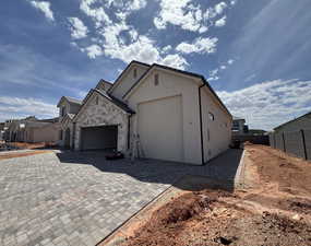 View of front facade with an attached garage, stucco siding, driveway, and stone siding