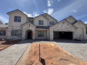 French country style house with stucco siding, decorative driveway, an attached garage, and stone siding