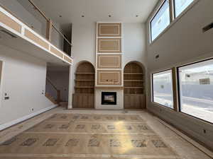 Unfurnished living room with built in shelves, a glass covered fireplace, plenty of natural light, and a high ceiling