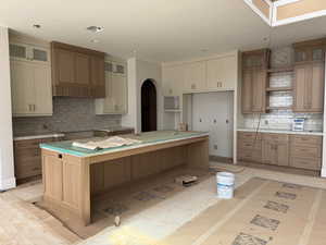 Dual tone kitchen with glass insert cabinets, open shelves, a kitchen island, backsplash, and arched walkways