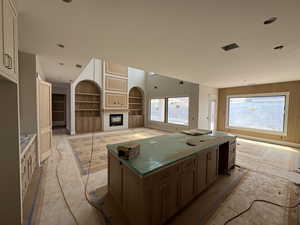 Kitchen featuring dual tone cabinets, open floor plan, a glass covered fireplace, a center island, and built in shelves