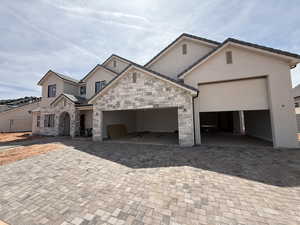 View of front of house with decorative driveway, an attached garage, stucco siding, and stone siding