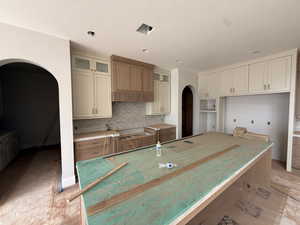 Kitchen featuring arched walkways, a center island, decorative backsplash, and glass fronted cabinets