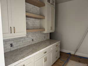 Kitchen with open shelves, glass fronted cabinets, tasteful backsplash, light countertops, and white cabinets
