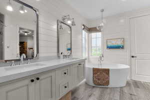 Ensuite bathroom featuring double vanity, light wood finished floors, wooden walls, and a freestanding tub