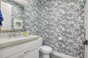 Half bath with wallpapered walls, vanity, and tile patterned flooring