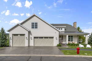 View of front of home featuring covered porch, a standing seam roof, concrete driveway, a chimney, and a front lawn