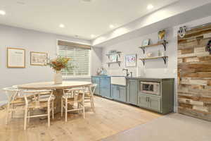 Bar area with dark countertops, open shelves, light wood-style flooring, stainless steel microwave, and recessed lighting