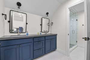 Bathroom featuring double vanity, vaulted ceiling, and a shower stall