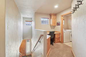 Corridor with an office area, a textured wall, light colored carpet, an upstairs landing, and independent washer and dryer