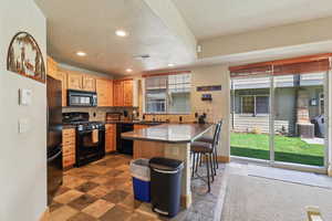 Kitchen with a peninsula, a breakfast bar, black appliances, tasteful backsplash, and light wood finish cabinets