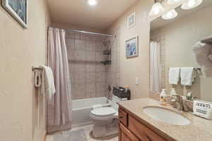 Full bath featuring a textured wall, vanity, light tile patterned flooring, and shower / tub combo with curtain