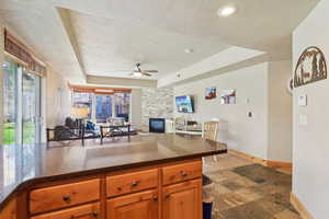 Kitchen featuring a raised ceiling, open floor plan, dark stone counters, light stone finish floors, and wood finish cabinets