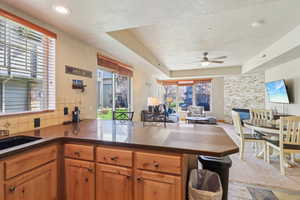 Kitchen featuring open floor plan, dark stone countertops, a peninsula, ceiling fan, and a tray ceiling