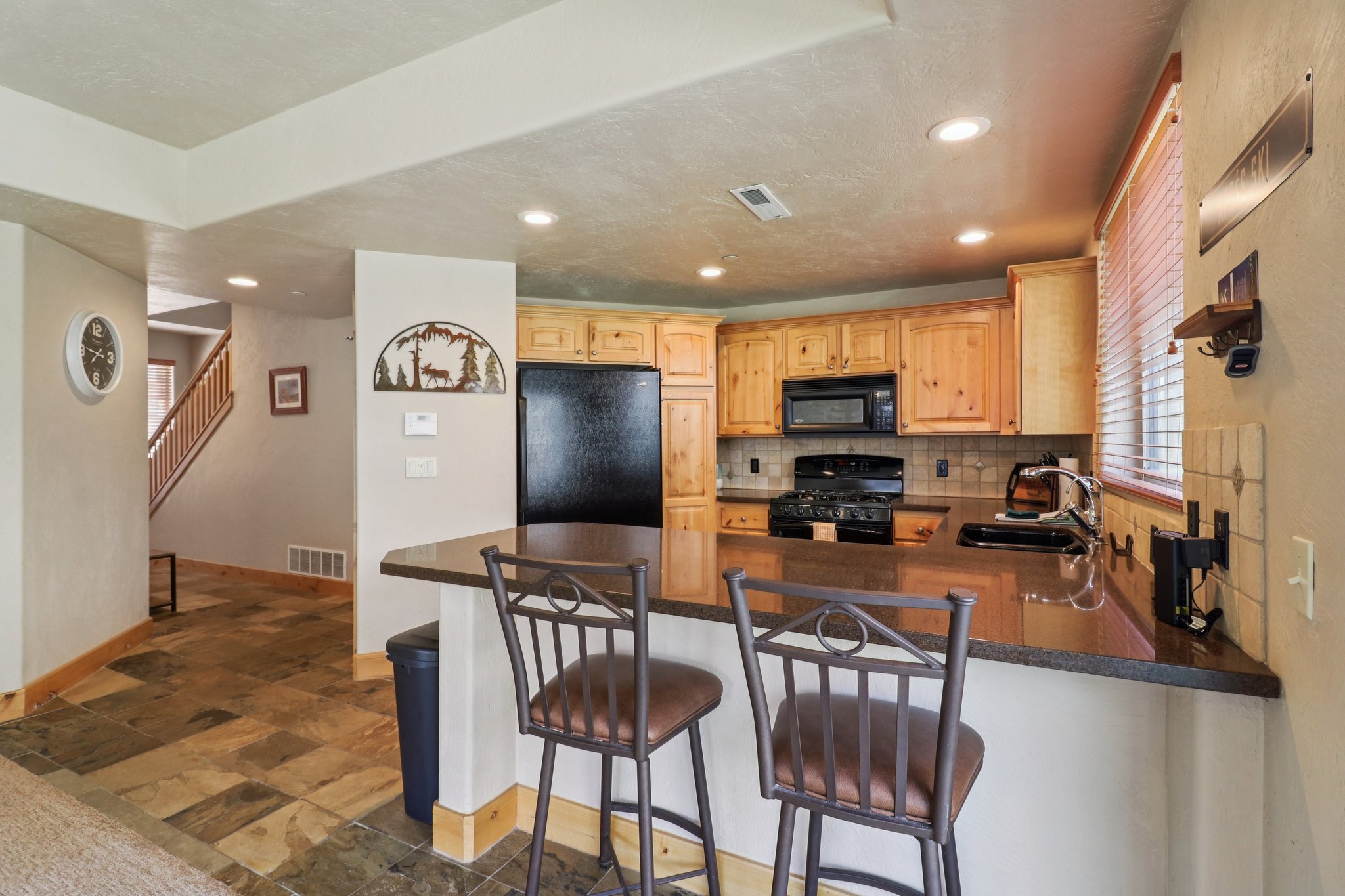Kitchen featuring black appliances, a peninsula, light wood finish cabinetry, a kitchen bar, and dark stone finish flooring