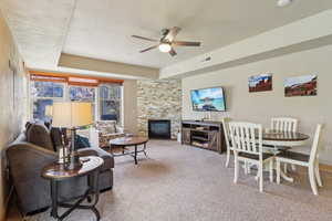 Carpeted living room featuring a ceiling fan, a fireplace, and a raised ceiling