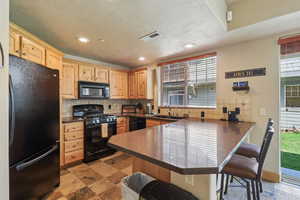 Kitchen with black appliances, a peninsula, a kitchen bar, light wood finish cabinetry, and recessed lighting