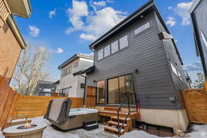 Back of house with a fenced backyard, a fire pit, and a hot tub