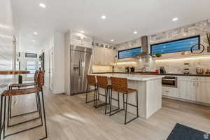 Kitchen with a kitchen bar, stainless steel built in fridge, a center island, light wood finished floors, and recessed lighting