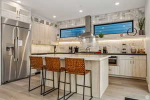 Kitchen with stainless steel appliances, light wood finish cabinets, a center island, range hood, and a breakfast bar area