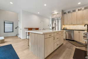 Kitchen featuring light wood finish cabinetry, a kitchen island, light wood-type flooring, glass insert cabinets, and stainless steel appliances