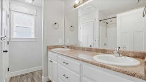 Primary bedroom full bath featuring double vanity, light wood finished floors, and a shower