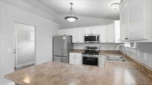 Kitchen featuring stainless steel appliances, white cabinetry, a peninsula, lofted ceiling, and hanging light fixtures