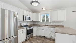 Kitchen with stainless steel appliances, white cabinetry, vaulted ceiling, a peninsula, and dark wood-type flooring