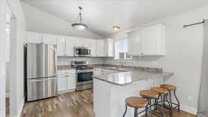 Kitchen with stainless steel appliances, a peninsula, a breakfast bar area, white cabinets, and vaulted ceiling