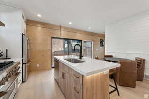 Kitchen with light wood finish cabinetry, a kitchen island with sink, modern cabinets, stainless steel appliances, and recessed lighting