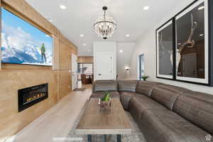 Living room featuring light wood-style flooring, a glass covered fireplace, and hanging lights