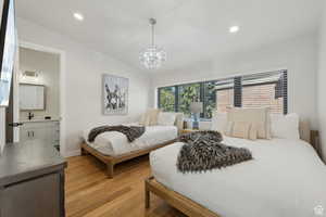 Bedroom featuring light wood finished floors, suspended lighting, lofted ceiling, and connected bathroom