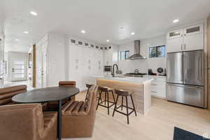 Kitchen with glass fronted cabinets, high end refrigerator, white cabinets, a kitchen bar, and a center island with sink