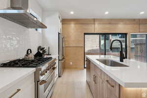 Kitchen featuring stainless steel appliances, light stone countertops, recessed lighting, a kitchen island with sink, and light wood-style floors