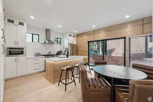 Dual tone kitchen with glass insert cabinets, a kitchen island with sink, light wood-style floors, high quality fridge, and two tone cabinets