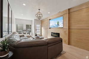 Living area featuring a chandelier, light wood-type flooring, a glass covered fireplace, a textured ceiling, and wooden walls