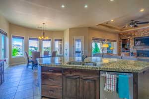 Kitchen with dark wood finish cabinetry, stainless steel dishwasher, open floor plan, a chandelier, and an island with sink