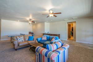 Living area with light colored carpet, a ceiling fan, and a textured ceiling