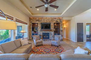 Living area featuring a ceiling fan, a fireplace, a raised ceiling, and tile patterned floors