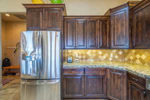 Kitchen with stainless steel fridge, dark wood finish cabinets, light stone countertops, and tasteful backsplash