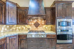 Kitchen featuring stainless steel appliances, dark wood finish cabinetry, light stone countertops, and decorative backsplash