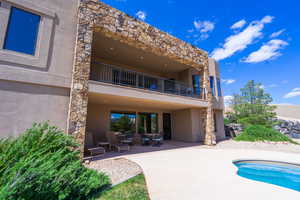 Back of property with stucco siding, stone siding, a patio, and a balcony