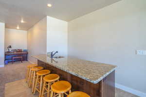 Kitchen with light stone counters, a breakfast bar area, recessed lighting, and light carpet
