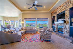 Living room with a ceiling fan, a fireplace, carpet floors, a raised ceiling, and plenty of natural light