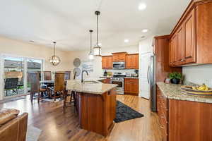 Kitchen with wood finish cabinetry, stainless steel appliances, an island with sink, light wood-style floors, and a breakfast bar area